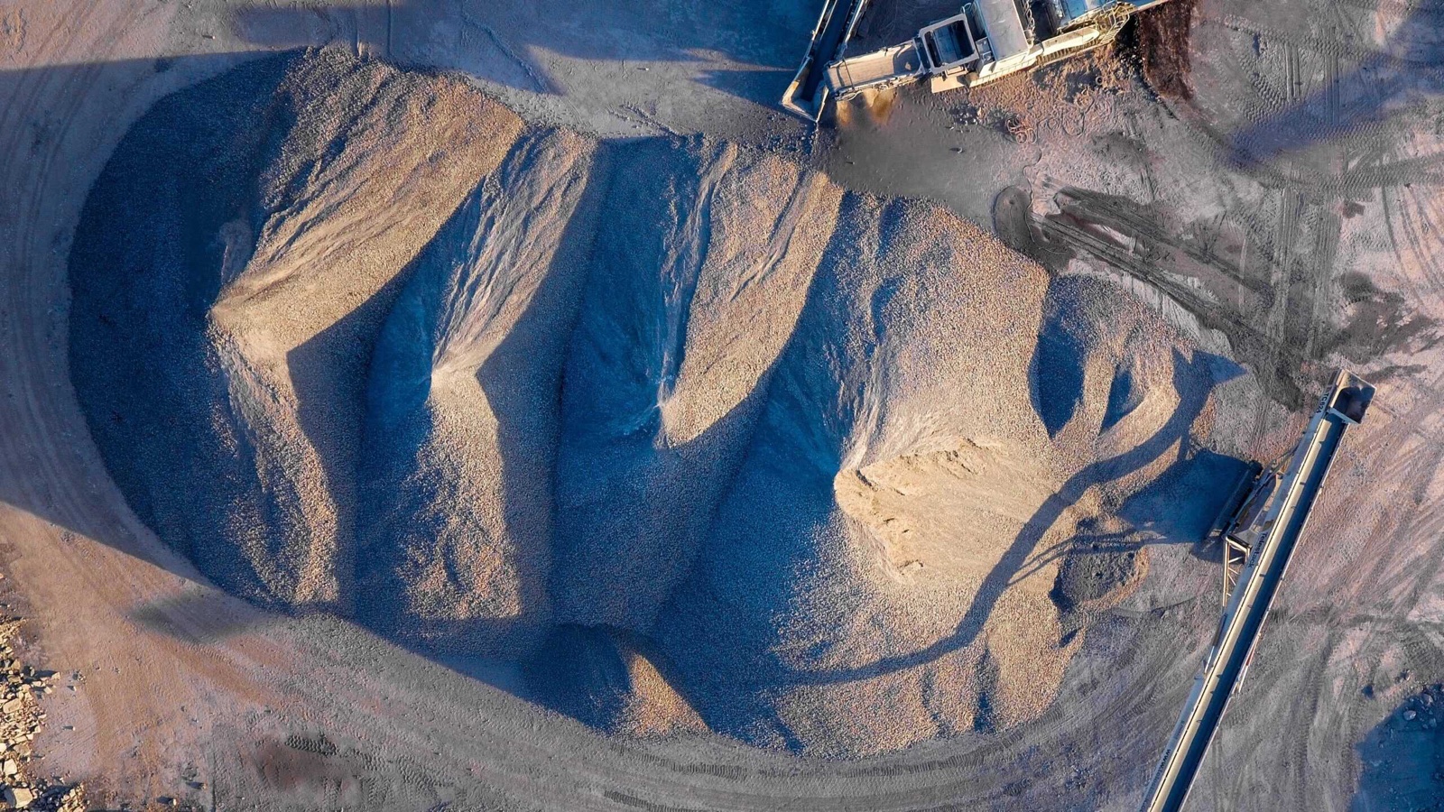 An aerial view of a large aggregate stockpile beside a conveyor.