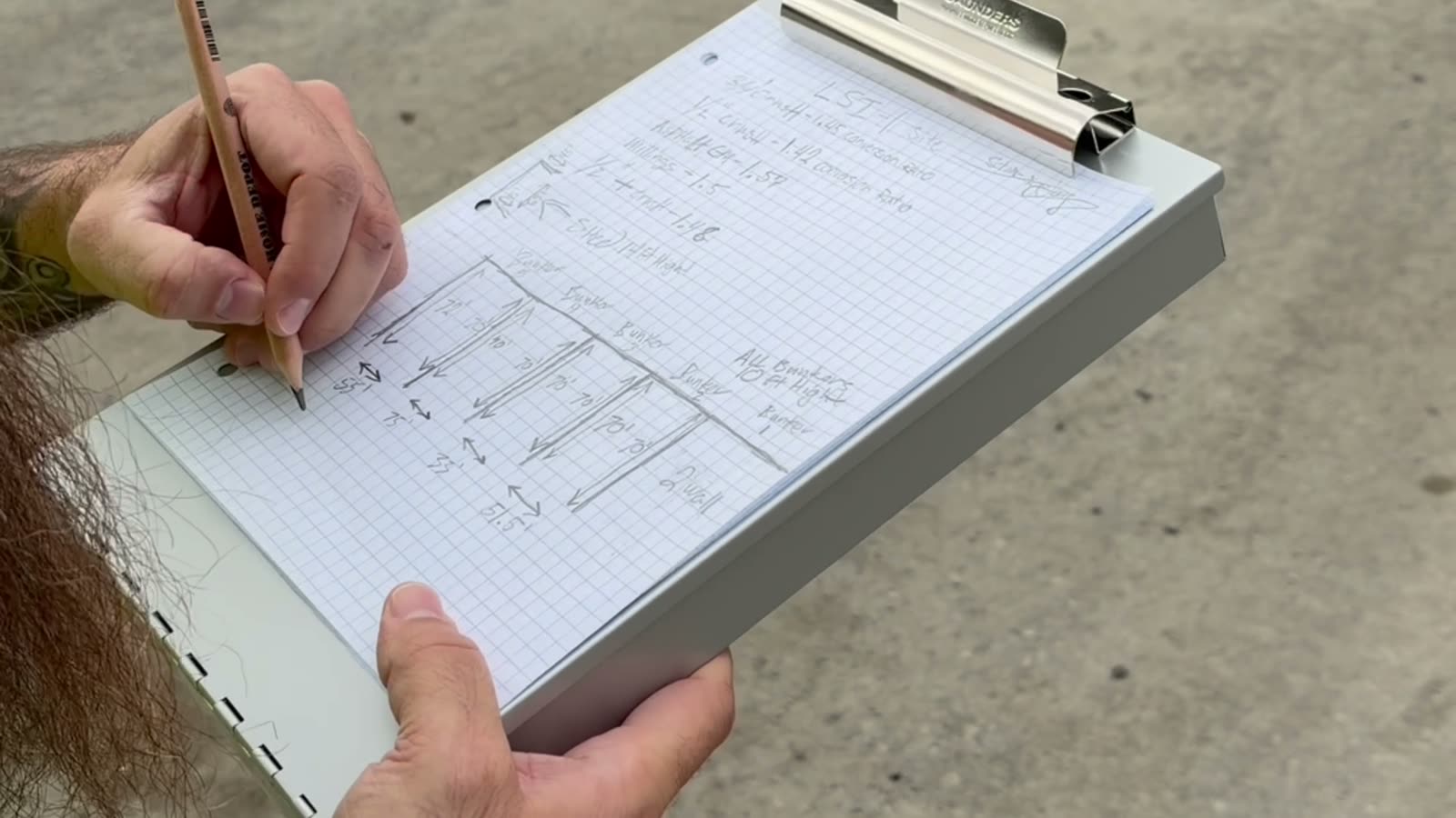 A hand sketches a yard of numbered stockpile bunkers on graph paper on a clipboard.